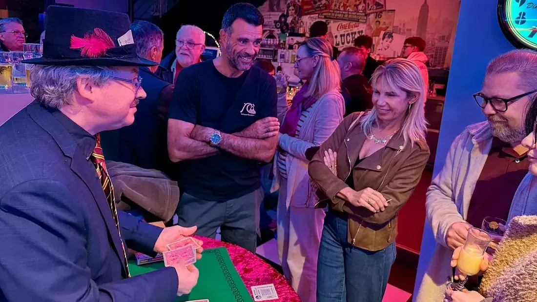 Sylvio le magicien présente un tour de cartes à un groupe de convives lors d'une soirée