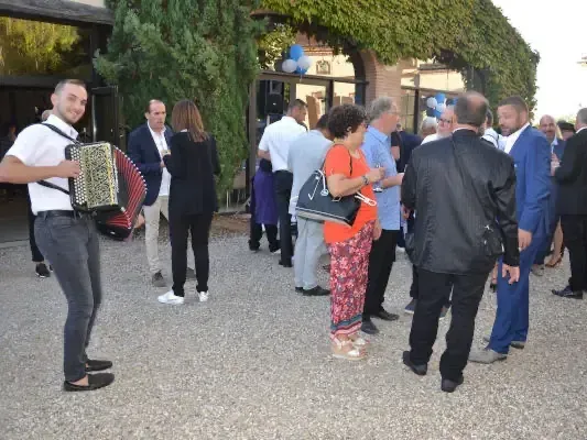 Un accordéoniste joue dans la cour d’un vin d’honneur, entouré d’invités en tenue de cérémonie