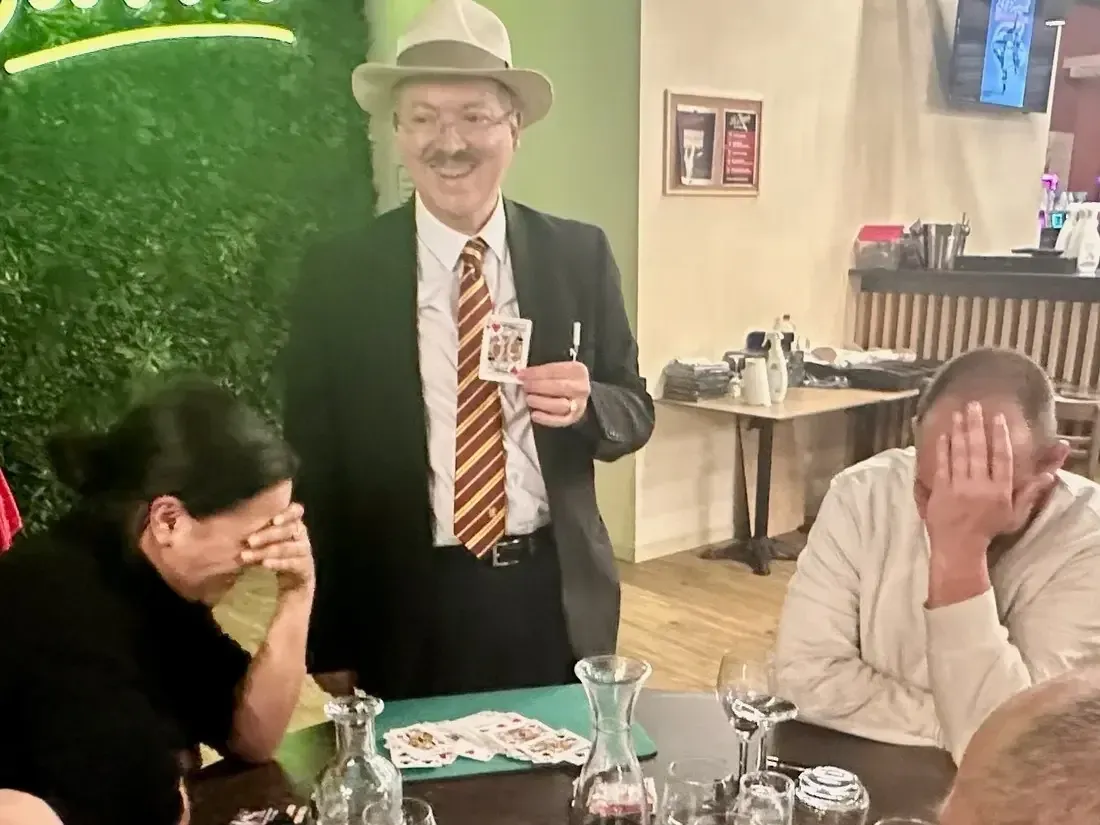 Sylvio, en veste bleu marine et cravate, une carte à la main, devant un comptoir de restaurant