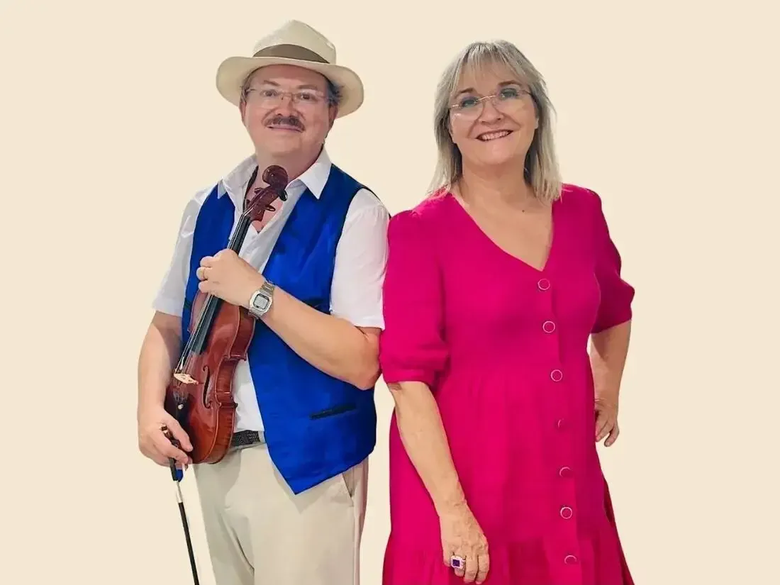 Sylvio, violon à la main, et Nathalie, chanteuse et conteuse, en robe rose, posent côte à côte