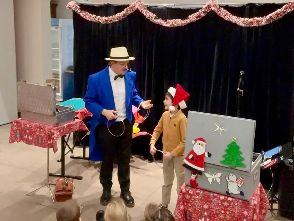 Spectacle de Noël : Sylvio le magicien en scène avec un enfant venu l'aider, décor de fête derrière eux
